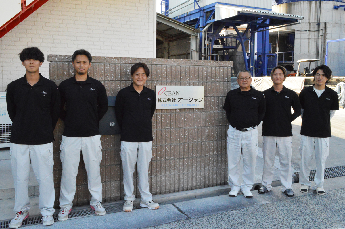 手の空いた若手スタッフの皆さんと社屋の前でパチリ。代表取締役社長の松永秀樹氏（右から3人目）、工場長の片岡正貴氏（左から3人目）、試験室の小芝泰祐さん（左から2人目）。